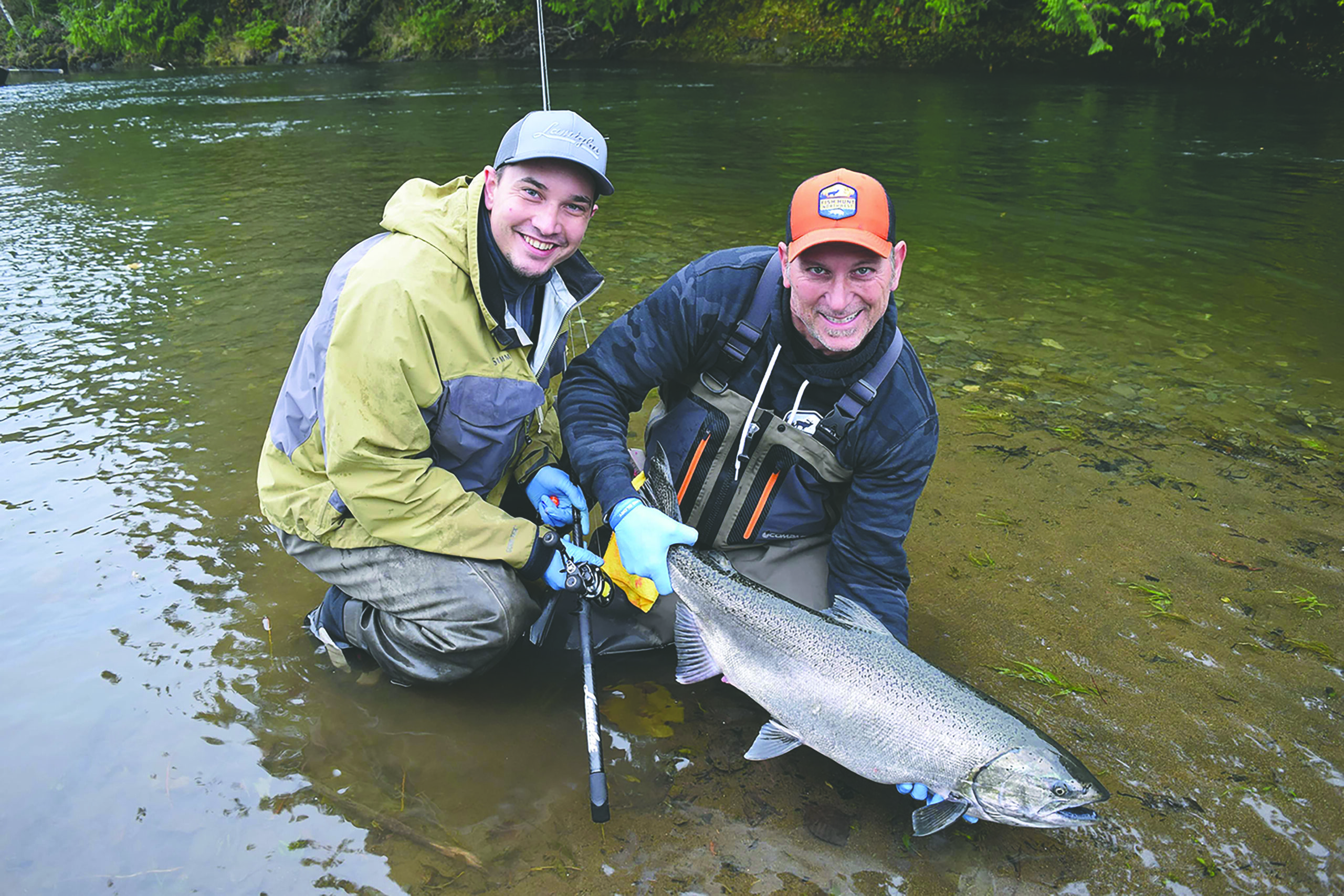 two men standing in a river holding up a fish