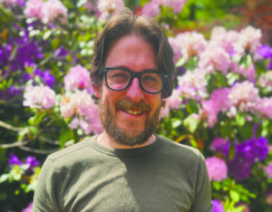 Justin Smiles for a photo in a garden of flowers