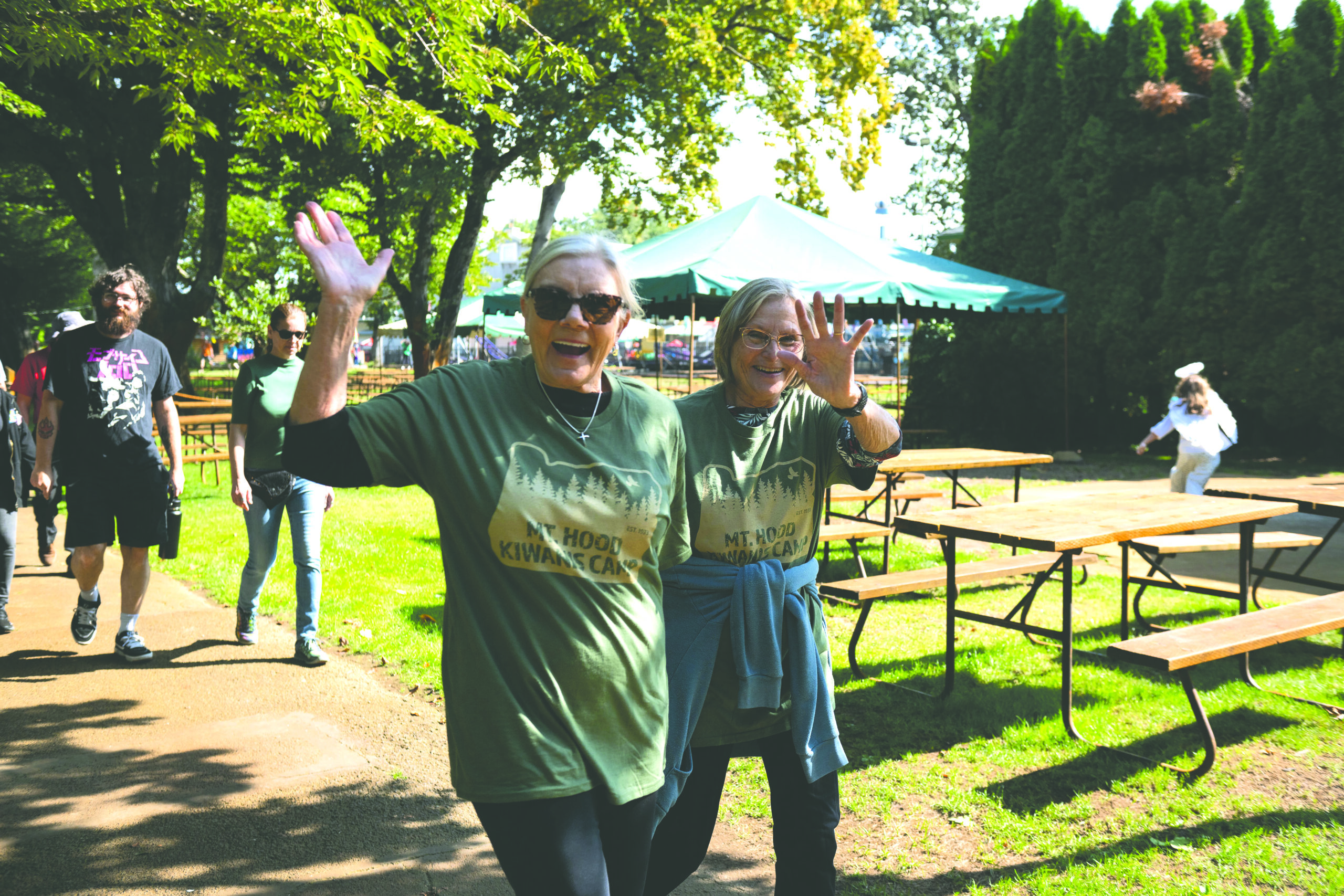 two friends wave at the camera as the go on a walk