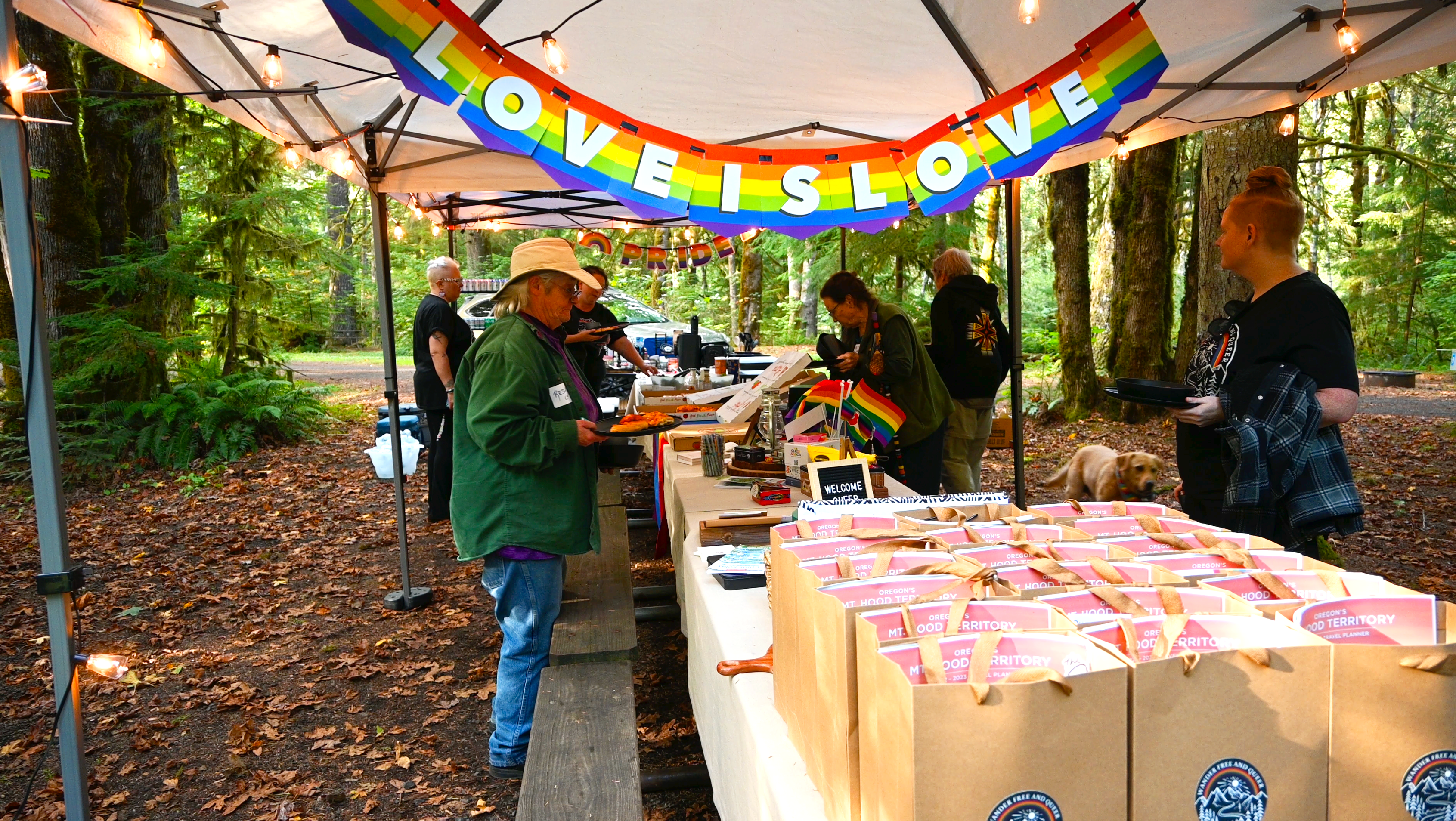 a picnic table of food with people gathering around