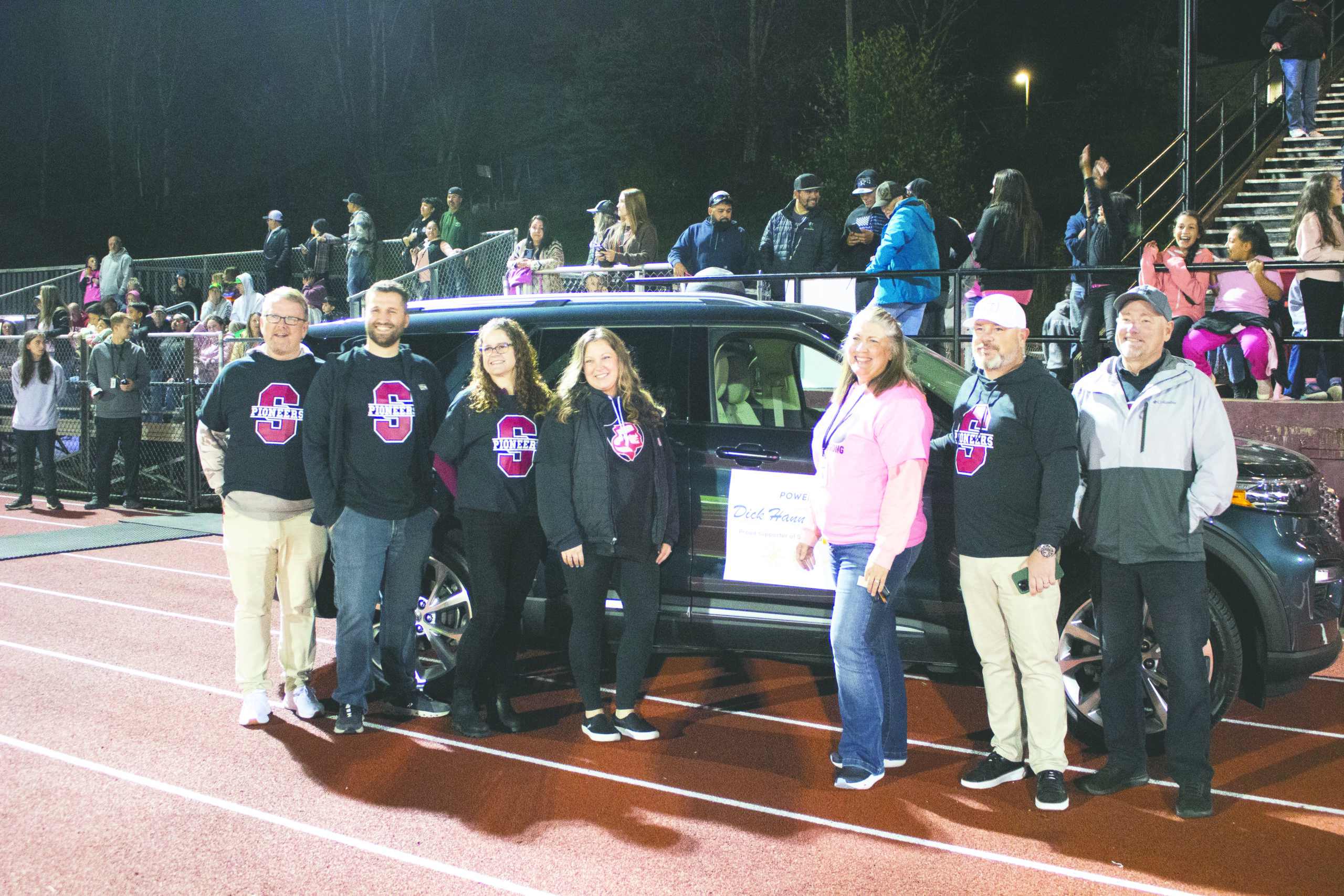 Dick Hannah and School staff pose in front of a car at a football game